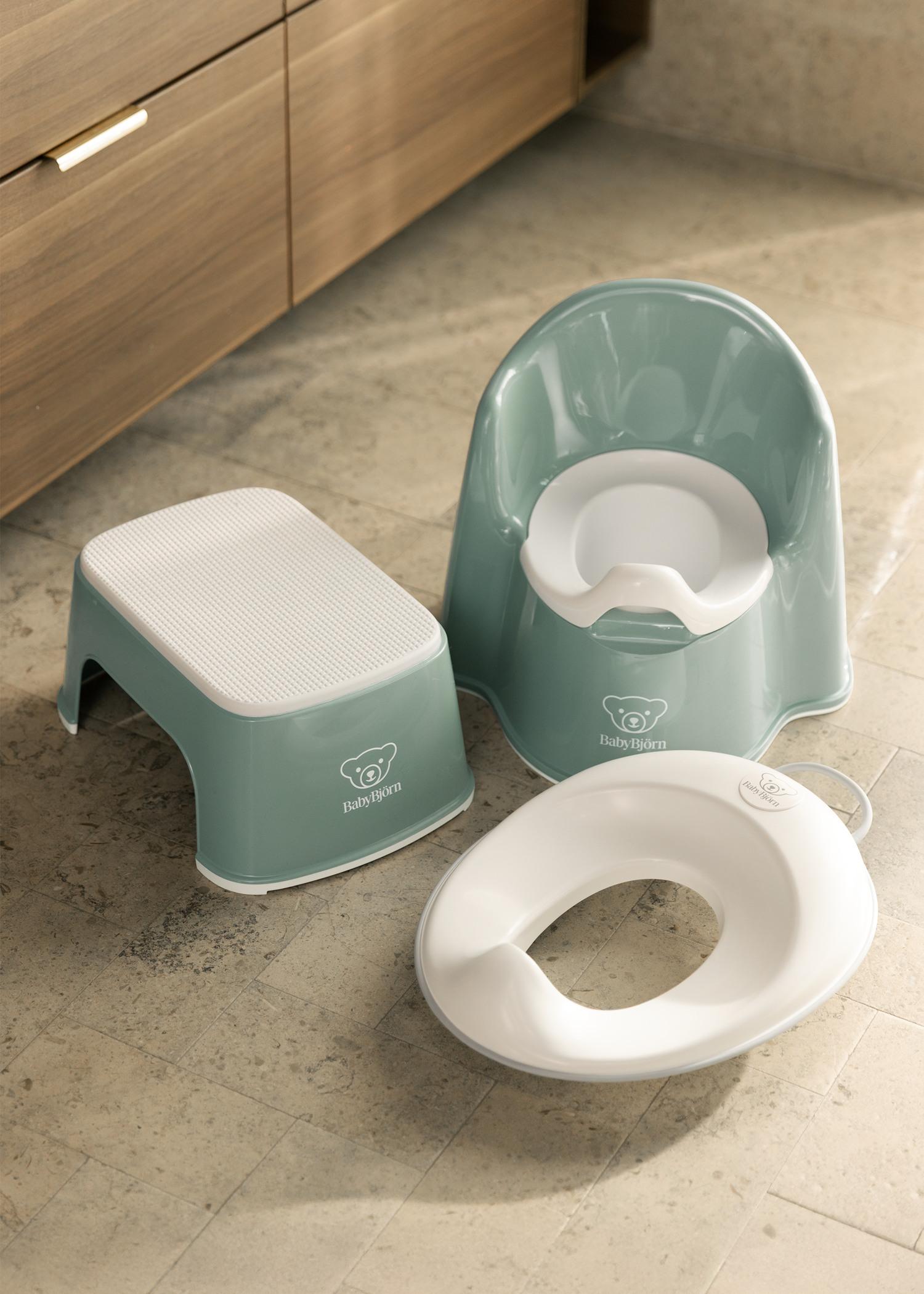 Children's bathroom set with a green potty chair, step stool, and white toilet training seat on a tiled floor.